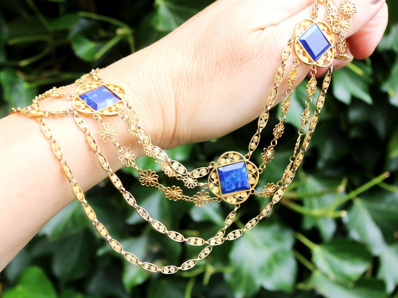 May include: A gold chain necklace with three strands and blue gemstone accents. The necklace features a delicate floral design.