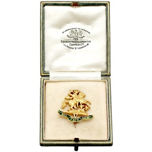 May include: A gold-colored pin in a green velvet box. The pin features a depiction of a knight on horseback, with the words "Quo Fata Vocant" inscribed on a banner below.
