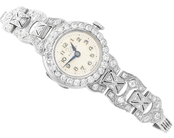 May include: A vintage silver wristwatch with a white face and diamond-encrusted band. The watch face has black Roman numeral hour markers and a blue hand. The watch face also has the text "Record Swiss Made".