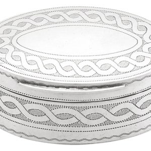 Puede incluir: Una caja de alhajas ovalada de plata con un diseño grabado decorativo. La caja tiene una tapa con bisagras y una superficie lisa y pulida.