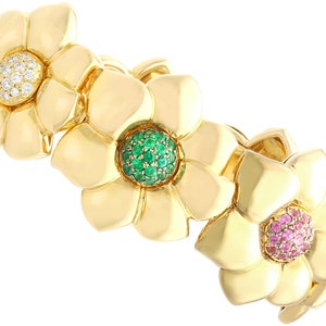 May include: A gold bracelet with three flower charms, each set with different colored gemstones. The first flower has white diamonds, the second has green emeralds, and the third has pink sapphires.