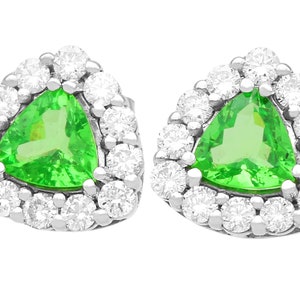 May include: A pair of green gemstone earrings with a triangular shape. Each earring is surrounded by a halo of smaller, round, white gemstones.