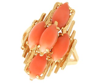 May include: A gold-toned ring featuring five oval, coral-colored gemstones. The gemstones are set in a textured, abstract gold frame. The ring has a wide band and a striking, eye-catching design.
