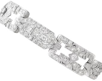 Puede incluir: Una pulsera plateada con un diseño geométrico, incrustada con numerosos diamantes pequeños y brillantes. La pulsera presenta eslabones rectangulares y en forma de diamante, creando un accesorio lujoso y elegante. El cierre también está adornado con diamantes.