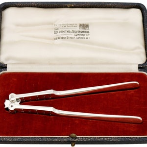 May include: Silver nutcracker in a red velvet lined box. The box is labeled "The Goldsmiths & Silversmiths Company Ltd. 112 Regent Street, London W.1."