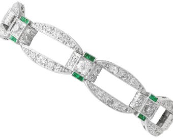Könnte beinhalten: Ein Platinarmband mit geometrischem Design. Das Armband verfügt über klare, rund geschliffene Diamanten und kleine, rechteckige Smaragd-Akzente. Die Glieder sind durch gebogene, diamantbesetzte Abschnitte verbunden.
