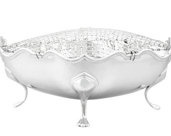 Op de afbeelding: Een zilverkleurige, ovaalvormige kom met een decoratief gaas inzetstuk. De kom heeft een geschulpte rand en wordt ondersteund door drie gebogen poten. Het ontwerp is elegant en vintage.