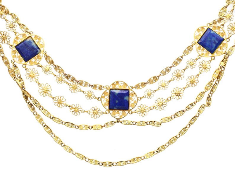 May include: A gold necklace with four strands of chain and four square lapis lazuli stones set in filigree. The necklace features a floral design.