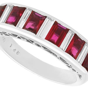 May include: A white gold band ring with five red ruby stones and small diamonds set in a decorative design.