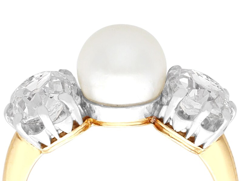 May include: A gold ring with a large white pearl in the center and two smaller diamonds on either side.