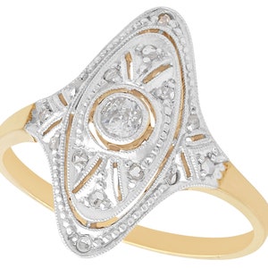 May include: A vintage-style gold ring with a delicate diamond design. The ring features a central diamond surrounded by smaller diamonds in a geometric pattern.