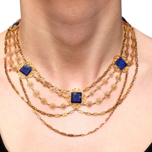 May include: A gold necklace with multiple strands and blue gemstone accents. The necklace features a delicate floral design and square-shaped stones.