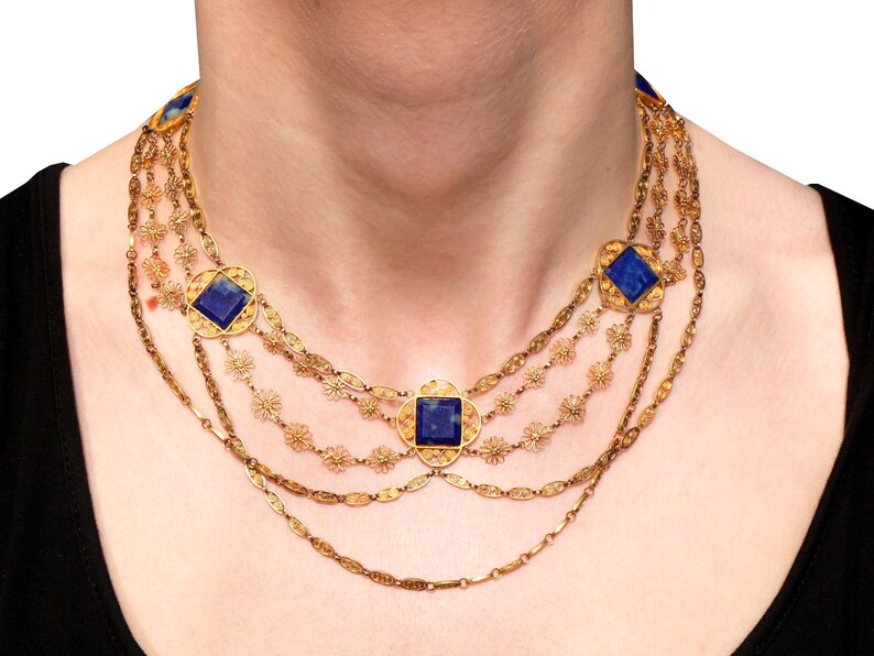 May include: A gold necklace with multiple strands and blue gemstone accents. The necklace features a delicate floral design and square-shaped stones.