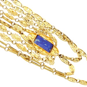 May include: A gold necklace with a blue stone pendant. The necklace is made of multiple strands of delicate, intricate chain links.