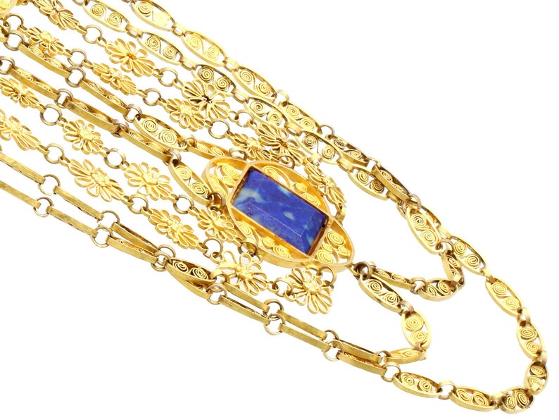 May include: A gold necklace with a blue stone pendant. The necklace is made of multiple strands of delicate, intricate chain links.