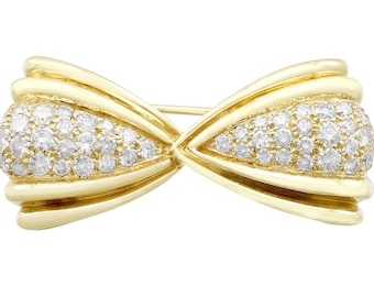 Op de afbeelding: Een gouden broche in de vorm van een strik met een pavé-zetting van kleine ronde diamanten.