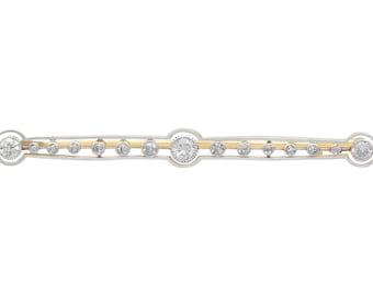 Op de afbeelding: Een delicate gouden en zilveren bar broche met een rij glinsterende diamanten.