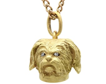 Op de afbeelding: Een gouden ketting met een hanger in de vorm van een gedetailleerd, getextureerd, driedimensionaal hondenhoofd met diamanten ogen.