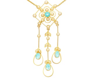 May include: A gold necklace with a pendant featuring a square design with a blue gemstone and pearl accents. The pendant has three dangling strands of pearls and blue gemstones.
