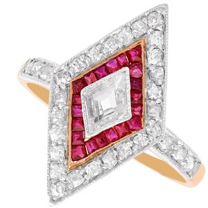 May include: A diamond-shaped ring featuring a central white diamond, surrounded by a border of square-cut red rubies, and an outer frame of small white diamonds set in metal. The ring band is a warm gold tone, contrasting with the silver-toned settings.