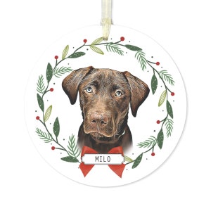 May include: A round Christmas ornament featuring a brown dog with a red bow and the name "MILO" on a white tag. The dog is surrounded by a green wreath with red berries.