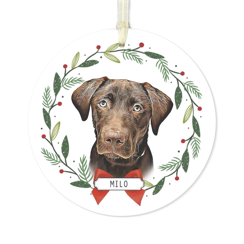 May include: A round Christmas ornament featuring a brown dog with a red bow and the name "MILO" on a white tag. The dog is surrounded by a green wreath with red berries.