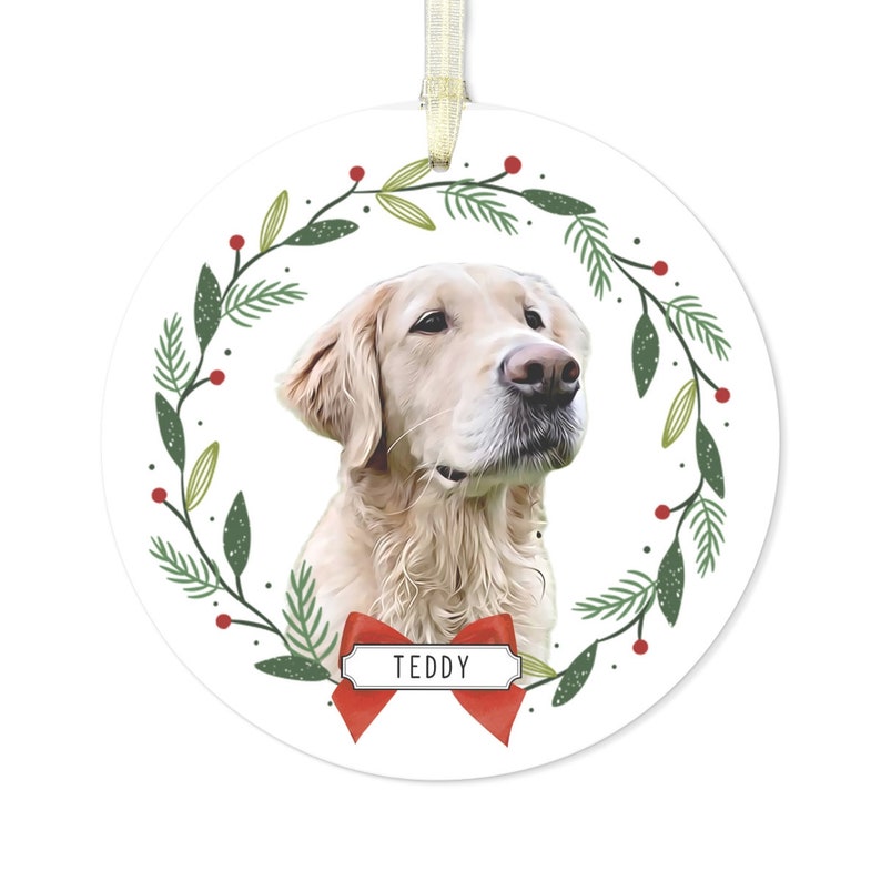 May include: A white round Christmas ornament with a green and red wreath design. A golden retriever dog is in the center of the wreath with the name "Teddy" on a red ribbon.
