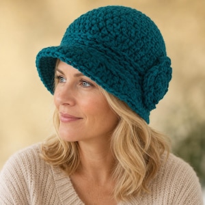 May include: A deep teal crochet cloche hat featuring a thick, textured yarn construction, a short brim, and a prominent circular crochet flower detail on the side. The hat is crafted with a dense, chunky stitch pattern that provides a structured shape.
