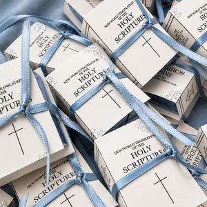 May include: A collection of small, white rectangular boxes, each tied with a light blue satin ribbon. The boxes feature the printed text New World Translation of the Holy Scriptures and a simple black cross symbol on the front cover.