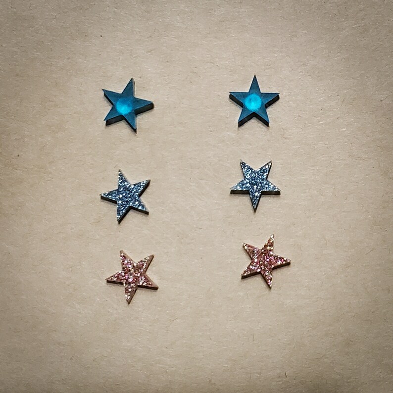 May include: Set of six star-shaped earrings. Two are blue with a glitter finish, two are silver with a glitter finish, and two are pink with a glitter finish.