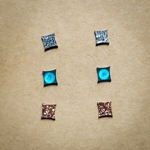 May include: Six pairs of square-shaped earrings with different glitter finishes. The earrings are silver, blue, and pink.
