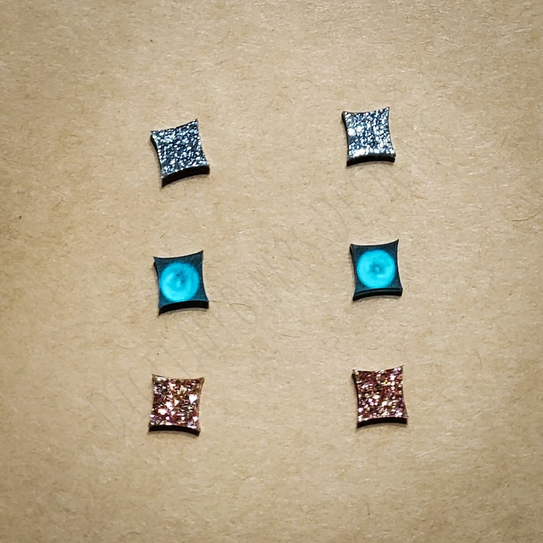 May include: Six pairs of square-shaped earrings with different glitter finishes. The earrings are silver, blue, and pink.