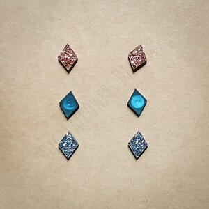 May include: Six pairs of diamond-shaped earrings. Two pairs are silver glitter, two pairs are blue glitter, and two pairs are pink glitter.