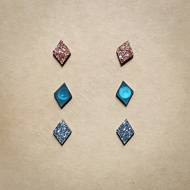 May include: Six pairs of diamond-shaped earrings. Two pairs are silver glitter, two pairs are blue glitter, and two pairs are pink glitter.