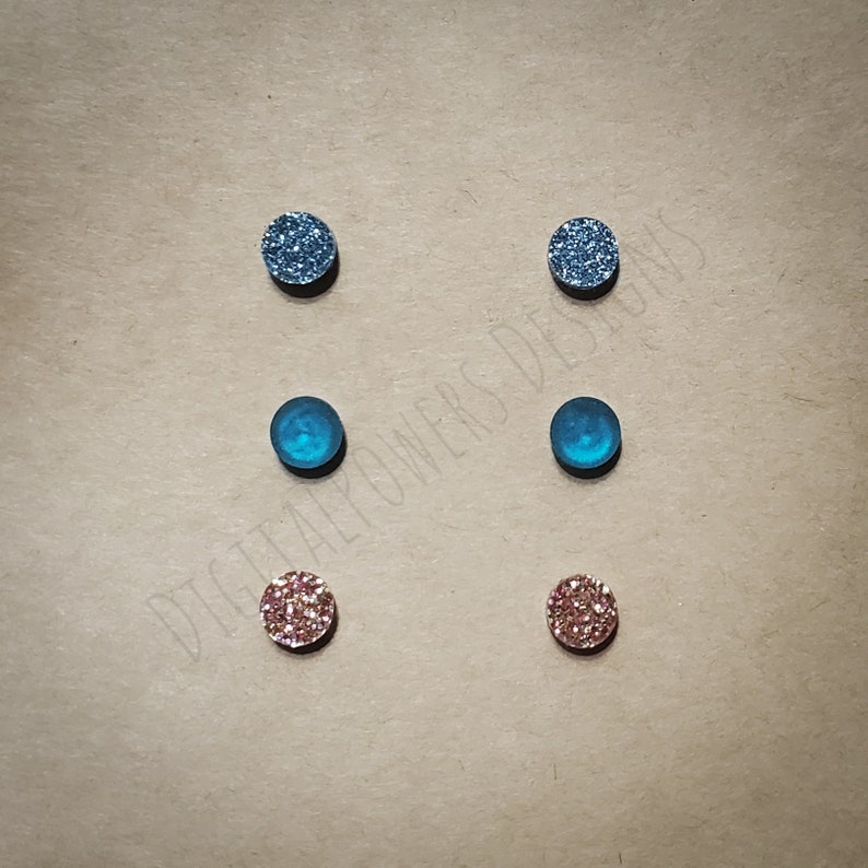May include: Set of six small round glitter earrings. Two are blue glitter, two are teal blue, and two are pink glitter.