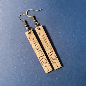 Puede incluir: Un par de pendientes de madera con un diseño de placa de circuito. Los pendientes son marrones y tienen ganchos dorados.