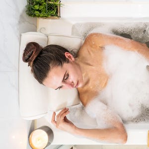 Bath pillow and bathtub tray set, the pillow from above: a woman rests her head on the roll headrest, both mesh panels in view.