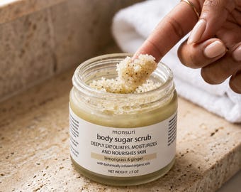 Peut inclure: Un pot en verre transparent contenant un gommage corporel au sucre Monsuri avec une étiquette blanche portant le texte : body sugar scrub, DEEPLY EXFOLIATES, MOISTURIZES AND NOURISHES SKIN, lemongrass & ginger, with botanically infused organic oils.
