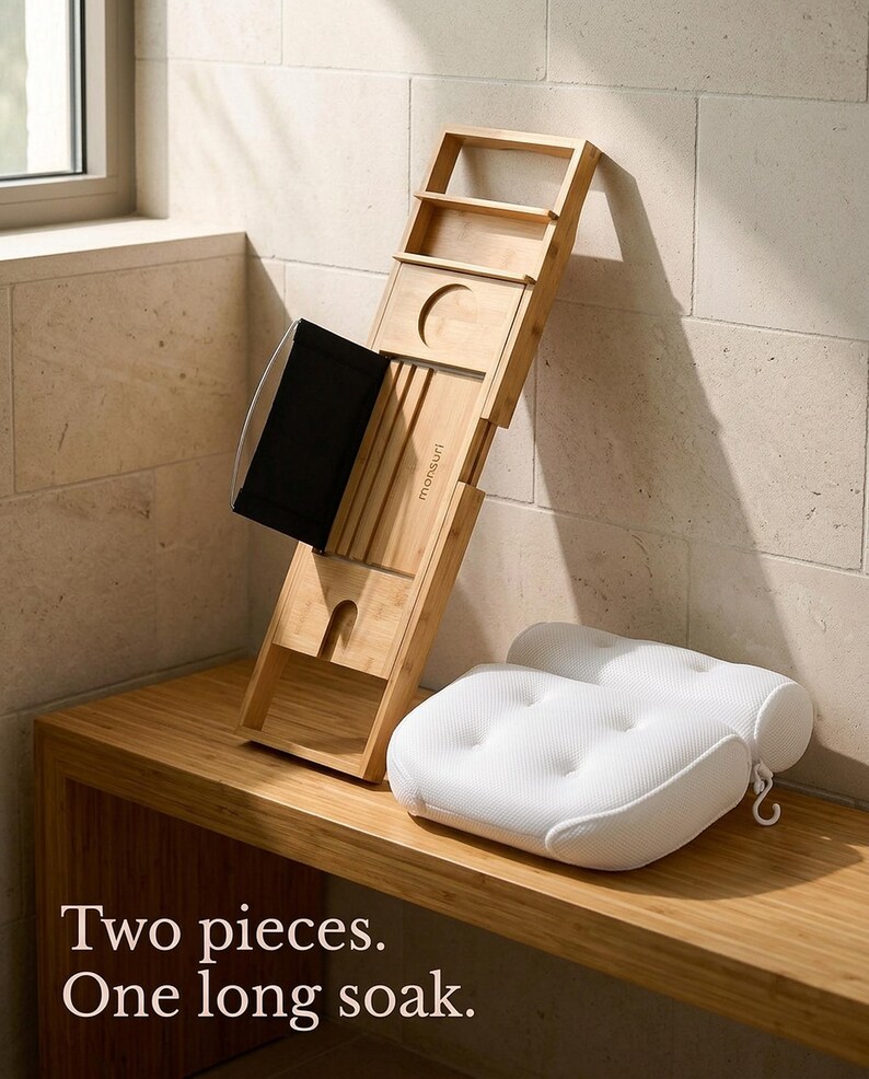 Bath pillow and bathtub tray set out of the tub: the bamboo tray leaning against a stone wall on a wooden bench and the mesh pillow beside it with its hanging hook, captioned Two pieces. One long soak.
