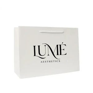 May include: A white paper shopping bag with a rectangular shape and a white cord handle. The bag features the black text "LUMÉ" above "AESTHETICS" in a stylized font.