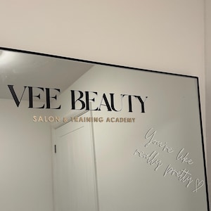 May include: A black-framed mirror with the text "VEE BEAUTY SALON & TRAINING ACADEMY" in gold lettering. The mirror also has the phrase "You're like really pretty" etched into the glass.