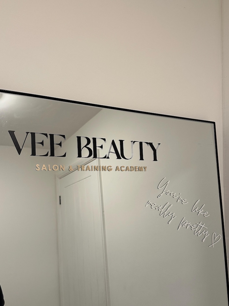 May include: A black-framed mirror with the text "VEE BEAUTY SALON & TRAINING ACADEMY" in gold lettering. The mirror also has the phrase "You're like really pretty" etched into the glass.