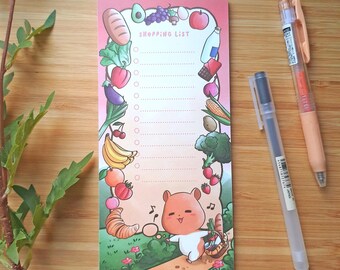 May include: A rectangular shopping list notepad with a pink gradient background. The notepad features a cartoon illustration of a hamster and various fruits and vegetables. The words "SHOPPING LIST" are printed at the top. Two pens are next to the notepad.