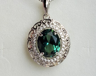 May include: A silver necklace with a green gemstone pendant surrounded by smaller clear gemstones in a decorative silver frame.