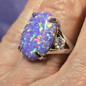 May include: A silver ring with a large oval-shaped purple opal gemstone and a smaller round clear gemstone. The ring is set in a silver band.
