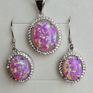 May include: A silver necklace and earrings set with pink opal stones surrounded by clear cubic zirconia stones.