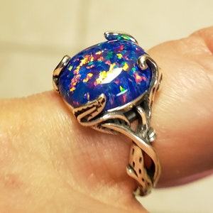 May include: A silver ring with a blue opal gemstone set in a floral design. The opal has iridescent flashes of color, including red, green, and gold.