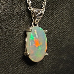 May include: A silver chain necklace with a silver pendant featuring a white opal gemstone with green and orange flashes.