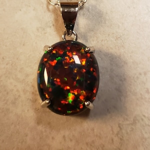 May include: A silver chain necklace with a black opal pendant. The opal has a dark background with flashes of green, red, and orange.