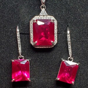 May include: A ruby and diamond necklace and earrings set. The necklace features a large, rectangular ruby pendant surrounded by smaller diamonds. The earrings are also rectangular and feature a ruby surrounded by diamonds.